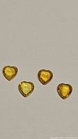 Four natural yellow sapphire gemstones laid flat on white background, heart cut shape visible, varying yellow hues and brilliance shown.