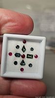 Collection of green-blue sapphires and red round rubies in presentation box held in hand, showing all stones.