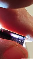 Close-up photo of octagon cut deep purple tourmaline held between fingers under light showing rich color and good transparency.