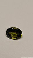 Oval cut vivid deep green peridot gemstone on a neutral background, showing facets and color.