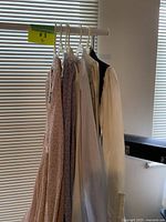 Six dresses hanging on a rack in front of blinds
