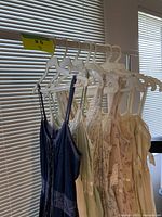 Seven spaghetti strap dresses hanging on rack by window
