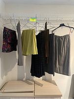 Seven vintage women's bottoms hanging on hangers on a wire rack, including skirts and pants in various colors and styles.