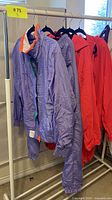 Side view of multiple vintage nylon tracksuit jackets hanging on rack; purple and red jackets visible