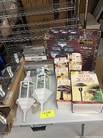 Box showing all lighting items together including outdoor lanterns, mushroom solar light 6-set, several boxed Malibu solar path lights, and Royal security lighting boxed floodlight.