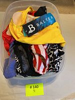 Plastic bin holding assorted vintage full piece bathing suits in various colors and patterns with Baltex label visible on yellow suit.