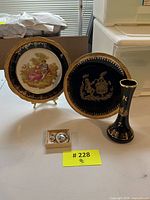 Two decorative plates and a black and gold vase, along with a small jewelry set displayed on a table.