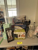 Photo of boxed kitchenware items including containers, coffee cups, utensils, and glass oil container.