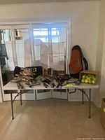 Full view of the tennis and badminton equipment laid on white table, including box of tennis balls and racket bag