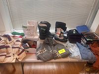 Full view of lot showing boots, sweaters, shirts, socks, toques, and suede jacket on table in daylight near window.