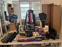 Wide view of the large lot showing golf bag, golf clubs, golf balls, baseballs, dumbbells, a golf clock, and boxed golf accessories displayed on a white folding table