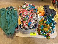 Lot contents overview with three containers of vintage beachwear items showing green swimsuits, colorful floral prints, leopard print and other patterned beachwear