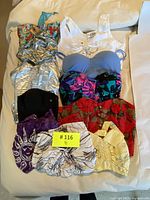 Ten vintage women's tops including bustiers and crop tops, laid out on a bed showing multiple colors and patterns