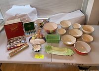 Full lot laid out on table showing ceramic bowls, fruit-themed dishes, steak knives, and teaspoons.