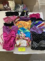 Overview of 11 suits laid out on table with additional bagged pieces in background