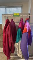Five vintage jackets and pants hanging on a metal rack, showing colors red, purple, teal and beige.