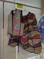 Two-piece batik skirt and vest set hanging on a rack in front of blinds under a label #99.