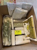 Box showing multiple white bed linens in original packaging including various sheet sets and folded linens.