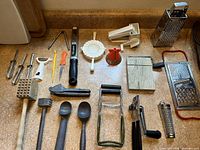 Photo of assorted grater, slicers, mallets, wooden and metal utensils including spatulas, cheese grater and metal scoop.