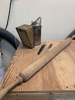 Bee smoker, rolling pin, and small knives on wooden surface