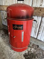 Full view of the red Brinkman electric smoker showing its cylindrical shape, domed lid with a handle, front access door with a temperature gauge, and side handles.