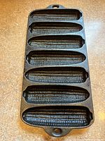 Cast iron corn-shaped pan with six corn molds for cooking corn-shaped food items.