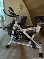 Side view of white and black exercise bike showing frame, flywheel and pedals with straps