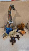 Photo of all eight animal figurines grouped, showing various colors, materials, and sizes including giraffe, dog, turtles, whale, elephant, and shark figurines.