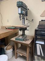 Full view of drill press mounted on wooden stand with surrounding workshop area