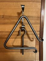 Full front view of iron dinner bell hung on mounting bracket against wood wall.