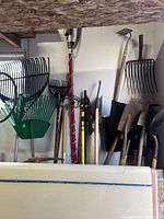 Wide view of assorted long-handled yard tools leaning against shed wall