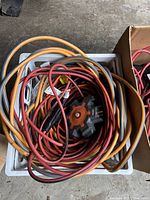 Top-down view of a crate filled with various extension cords in red, orange, and black colors, including a multi-outlet adapter with orange accents.