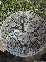 Top view of metal sundial featuring zodiac signs and compass rose in the center, showing weathering and some rust spots.