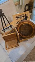 Photo displaying a small wooden box with hinged lid, a medium wooden Yukon Jack box, a small wooden easel, and a round wooden clock with glass and rope detail.