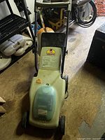 Front view of the beige/green Neuton electric lawn mower showing the body and wheels on a concrete floor.