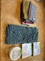 Photo of folded microfiber towels (green, gray, burgundy) and chenille microfiber towel. Also visible two boxes: Norwex Cleaning Paste container and two boxed items (Spirisponges and Micro Cleaning Hand Pads).