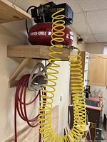 Porter-Cable air compressor with yellow coiled hose and red long hose on wooden shelf in workshop.
