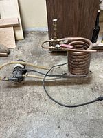 Full view of pump assembly with electric motor, copper coil, valves, and hoses against garage floor.