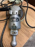 View showing the electric polisher lying on a wooden surface with attached power cord and polishing head.