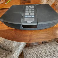 Front view of black Bose Wave Radio showing digital display and top control buttons on wooden surface.