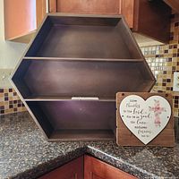 Photo of dark wood octagonal hanging shelf next to small religious plaque on kitchen counter