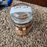 Glass jar with screw-top lid containing many pennies inside, placed on carpet.