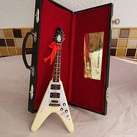 Miniature Gibson Flying V guitar inside black hard case with red plush lining and Certificate of Authenticity visible.