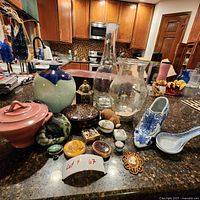 Multiple decorative items including ceramic vases, porcelain soup spoons, blue and white ceramic shoe, pink candle dish, collectible boxes, and garden fairy light on kitchen counter surface.
