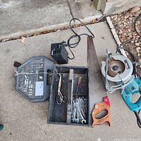 Overview photo showing ratchet set, hand saw, circular saw, power converter, scissors and wrenches laid out on a concrete surface