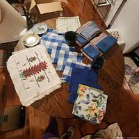 Overhead view of assorted placemats, cloth napkins, two small vases, and two decorative plates spread on wooden table.