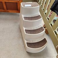 Plastic pet steps with carpeted treads in white plastic with brown carpet on each step, showing paw print design on the edges.