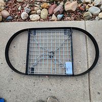 Oval metal pot hanging rack with black frame and chains lying on concrete