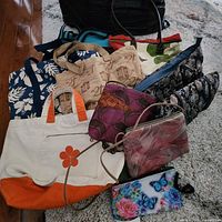 Photo of all 10 bags and purses together on carpet and floor showing variety of colors and styles.