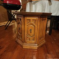 Photo of the wooden hexagonal side table showing the paneled sides and decorative molding with metal pull handles.